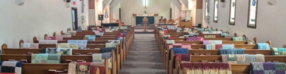 A picture of the sanctuary with many blankets laid over the pews to show our set up for our sewing group blanket sale to support CLWR